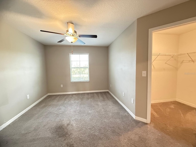 unfurnished bedroom with carpet, ceiling fan, a textured ceiling, a spacious closet, and a closet