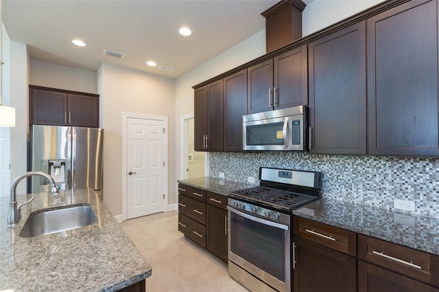 kitchen with dark stone counters, stainless steel appliances, backsplash, and sink