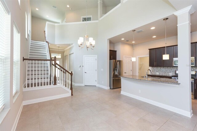 kitchen featuring light tile patterned flooring, light stone countertops, a towering ceiling, appliances with stainless steel finishes, and backsplash