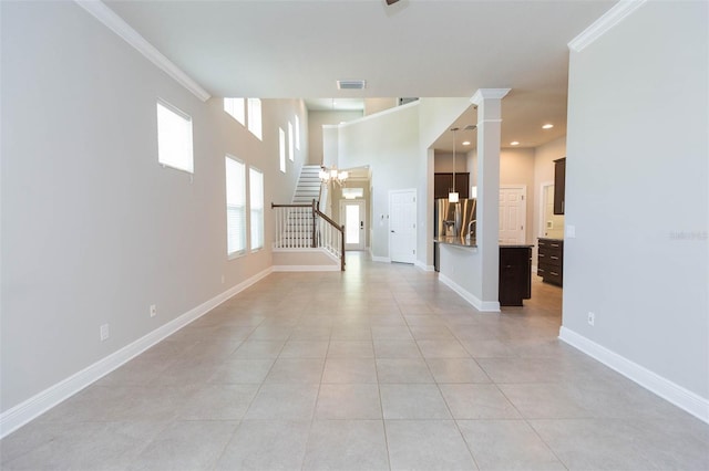 unfurnished room with a notable chandelier, decorative columns, light tile patterned floors, a towering ceiling, and ornamental molding