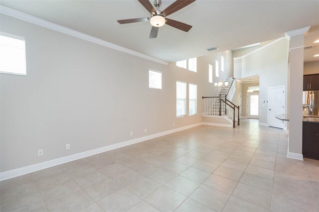 unfurnished room with a high ceiling, ceiling fan with notable chandelier, light tile patterned floors, and crown molding