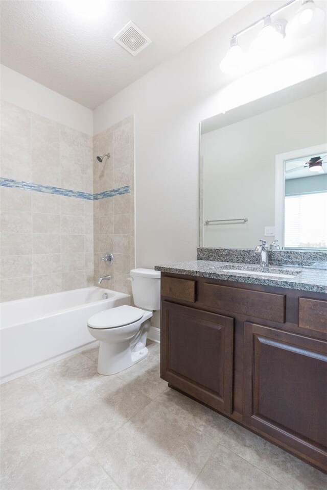 full bathroom featuring tile patterned flooring, a textured ceiling, toilet, vanity, and tiled shower / bath combo