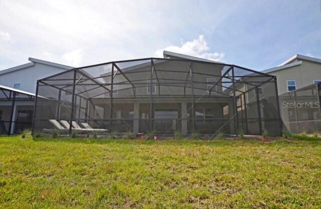 rear view of house with a yard and glass enclosure