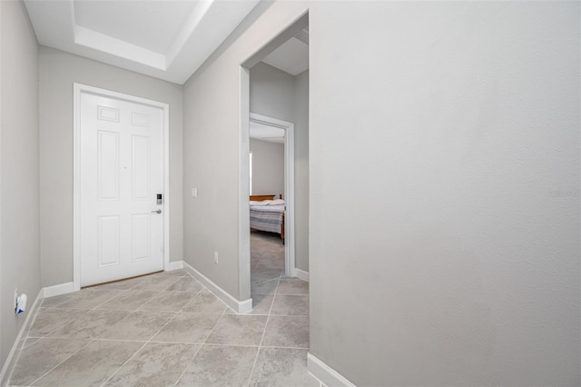 hallway featuring light tile patterned floors and a tray ceiling