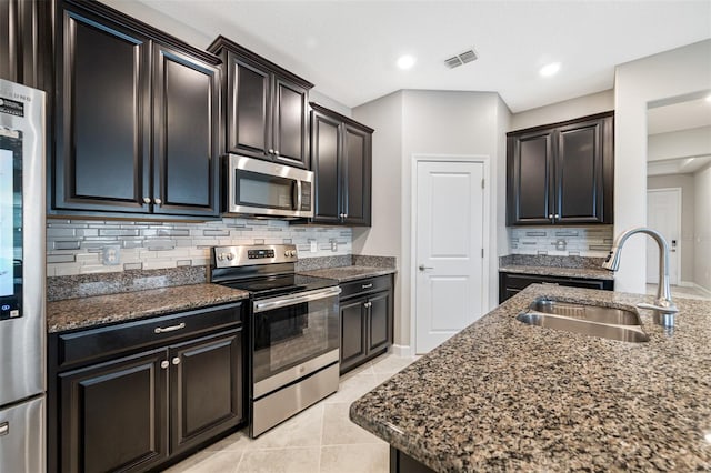 kitchen featuring dark stone counters, stainless steel appliances, decorative backsplash, sink, and light tile patterned floors