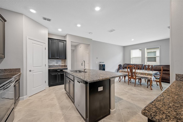 kitchen with light tile patterned flooring, stone counters, an island with sink, sink, and electric range oven