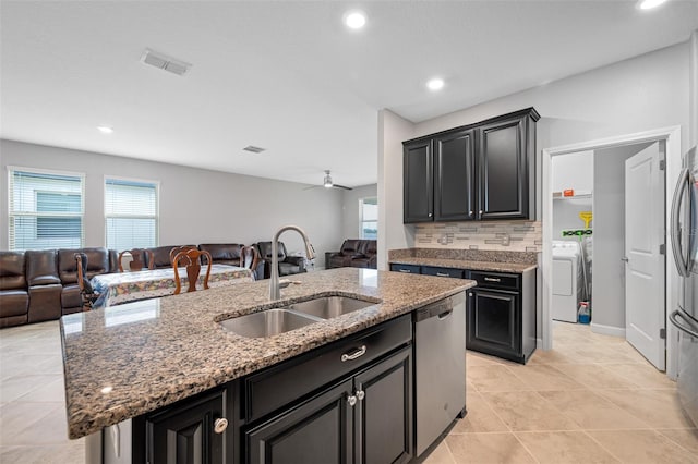 kitchen featuring tasteful backsplash, a center island with sink, ceiling fan, light stone countertops, and sink