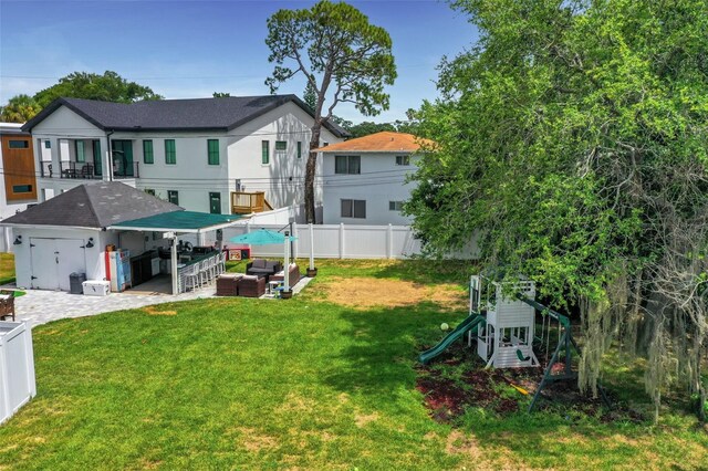 rear view of property featuring an outdoor living space, a patio area, a playground, a lawn, and exterior bar