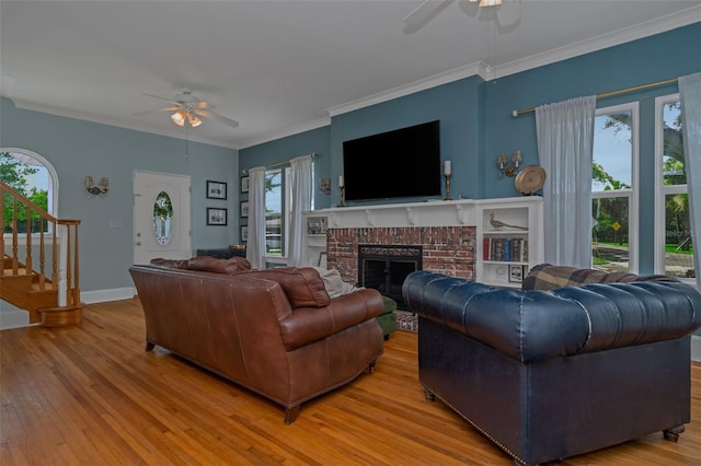 living room featuring ceiling fan, hardwood / wood-style floors, crown molding, and a fireplace