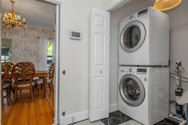 laundry area with stacked washer and dryer, ornamental molding, and a notable chandelier