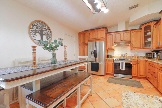 kitchen featuring light tile patterned flooring, tasteful backsplash, vaulted ceiling, and stainless steel appliances