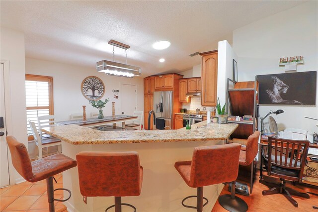 kitchen with a breakfast bar, vaulted ceiling, kitchen peninsula, stainless steel appliances, and decorative light fixtures