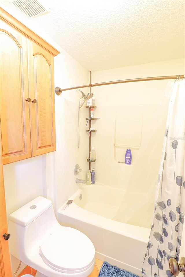 bathroom with tile patterned flooring, shower / bath combo with shower curtain, toilet, and a textured ceiling