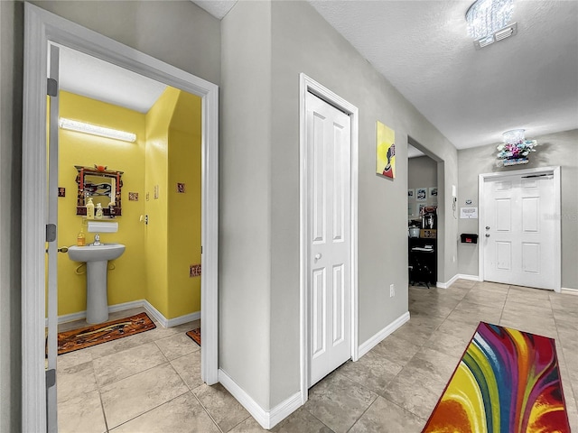 corridor with light tile patterned floors, a textured ceiling, and sink