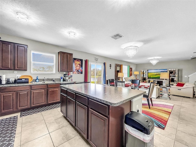 kitchen featuring light tile patterned flooring, a kitchen island, a textured ceiling, sink, and a chandelier