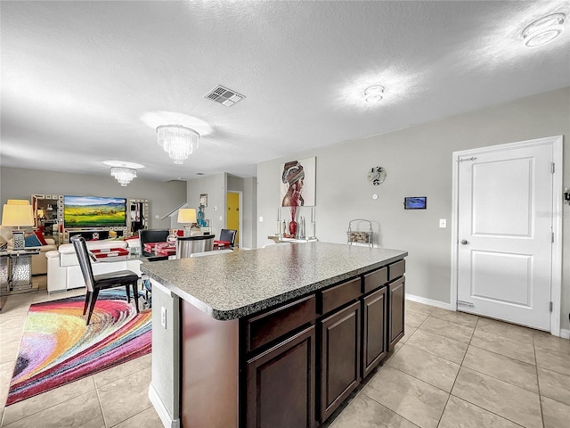 kitchen featuring light tile patterned flooring, a textured ceiling, dark brown cabinets, a chandelier, and a kitchen island