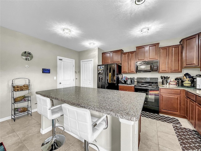 kitchen with light tile patterned flooring, black appliances, a breakfast bar area, a textured ceiling, and a kitchen island