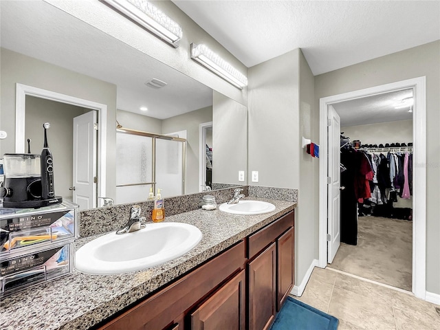 bathroom featuring tile patterned flooring, vanity, a textured ceiling, and a shower with door