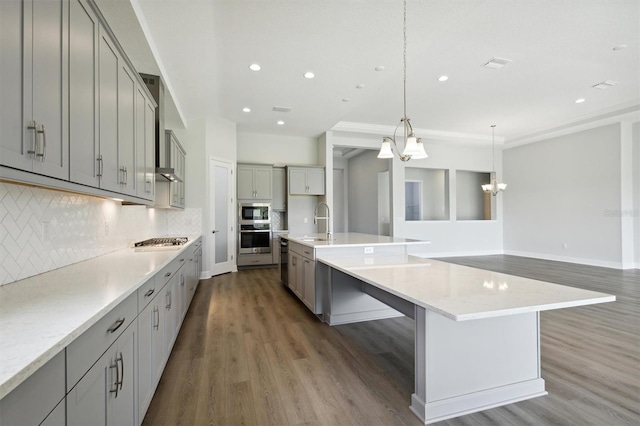 kitchen featuring a large island with sink, dark wood-type flooring, backsplash, pendant lighting, and appliances with stainless steel finishes