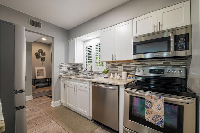 kitchen featuring appliances with stainless steel finishes, white cabinetry, sink, backsplash, and light stone countertops