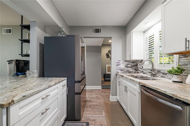 kitchen with sink, appliances with stainless steel finishes, backsplash, light stone counters, and white cabinets