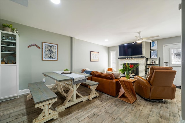 living room featuring ceiling fan, hardwood / wood-style floors, and a brick fireplace