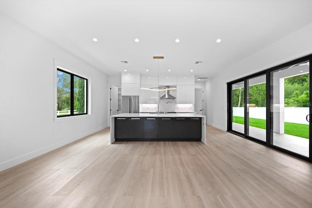 kitchen featuring white cabinetry, a kitchen island with sink, decorative backsplash, pendant lighting, and wall chimney exhaust hood