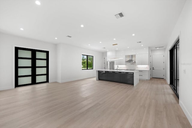 kitchen featuring tasteful backsplash, white cabinetry, a large island, wall chimney range hood, and light hardwood / wood-style flooring