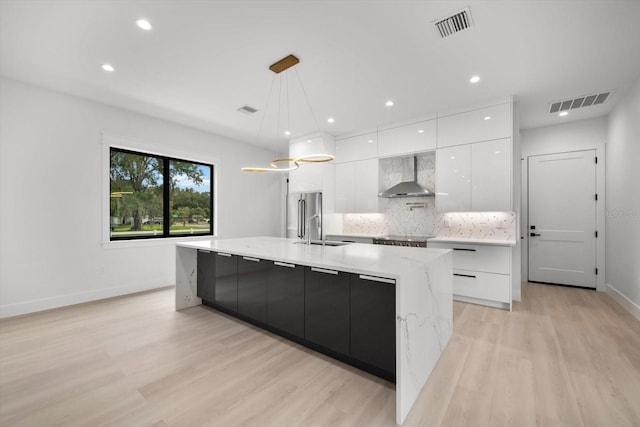 kitchen with white cabinetry, hanging light fixtures, a large island, decorative backsplash, and wall chimney exhaust hood