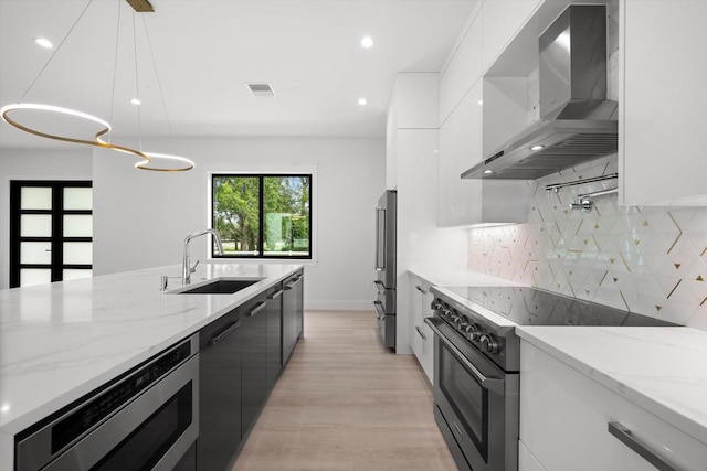 kitchen featuring wall chimney exhaust hood, white cabinetry, hanging light fixtures, and appliances with stainless steel finishes