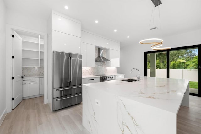 kitchen with decorative light fixtures, wall chimney range hood, white cabinetry, stainless steel appliances, and sink