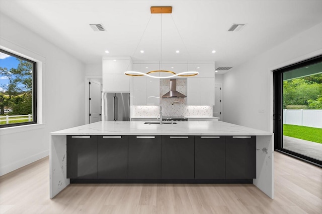 kitchen featuring decorative light fixtures, wall chimney exhaust hood, white cabinetry, decorative backsplash, and high quality fridge