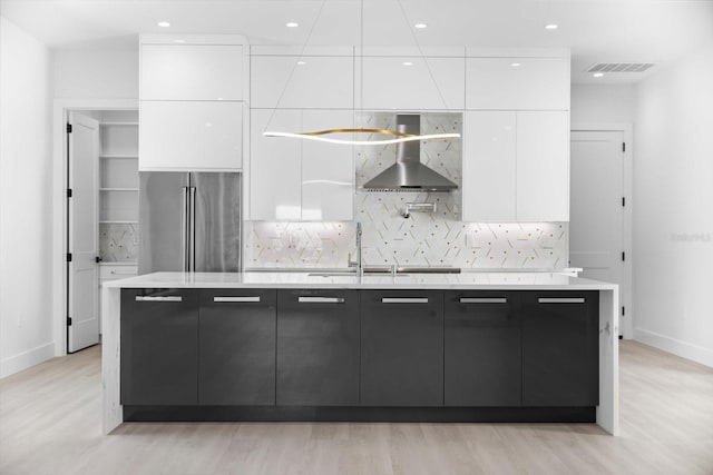 kitchen with white cabinets, tasteful backsplash, high end fridge, a kitchen island with sink, and wall chimney range hood