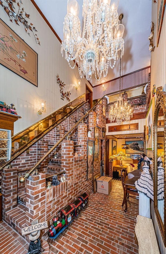 wine area featuring crown molding, a towering ceiling, brick wall, and a chandelier