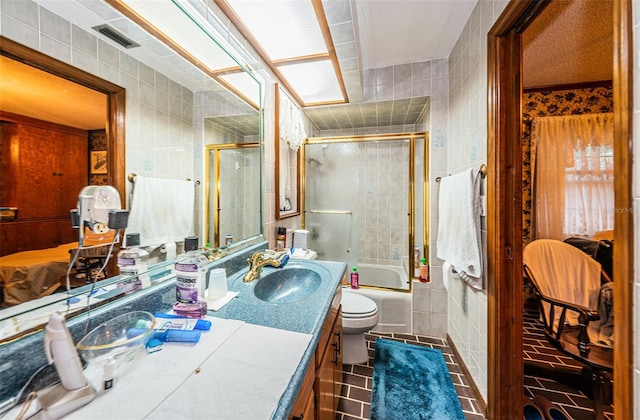 full bathroom featuring tile patterned floors, toilet, bath / shower combo with glass door, tile walls, and vanity