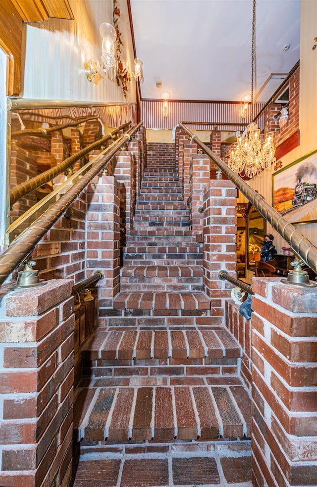 staircase featuring brick wall and an inviting chandelier