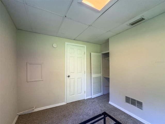 empty room with a paneled ceiling and dark colored carpet