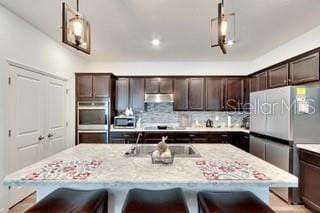 kitchen featuring dark brown cabinetry, decorative light fixtures, a breakfast bar, and a center island with sink