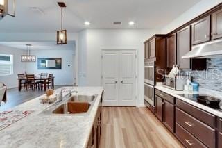 kitchen featuring sink, hanging light fixtures, dark brown cabinetry, light stone countertops, and light hardwood / wood-style flooring