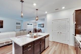 kitchen with sink, hanging light fixtures, stainless steel dishwasher, dark brown cabinetry, and a center island with sink