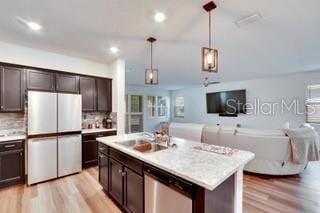 kitchen featuring sink, decorative light fixtures, fridge, stainless steel dishwasher, and a kitchen island with sink