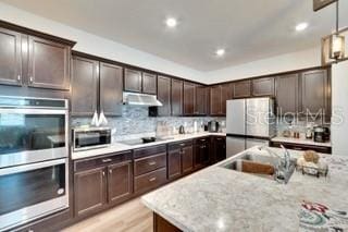 kitchen with dark brown cabinetry, backsplash, light stone countertops, and appliances with stainless steel finishes