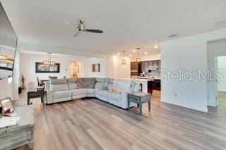 living room with ceiling fan with notable chandelier and light wood-type flooring