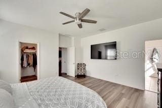 bedroom featuring a walk in closet, dark wood-type flooring, and ceiling fan