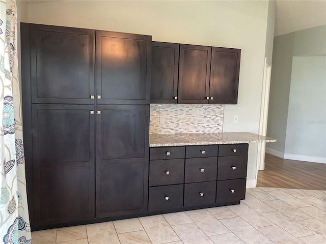 kitchen with dark brown cabinets, backsplash, and light stone counters