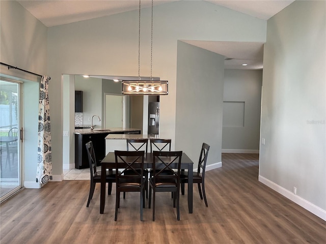 dining area featuring sink, wood-type flooring, and high vaulted ceiling