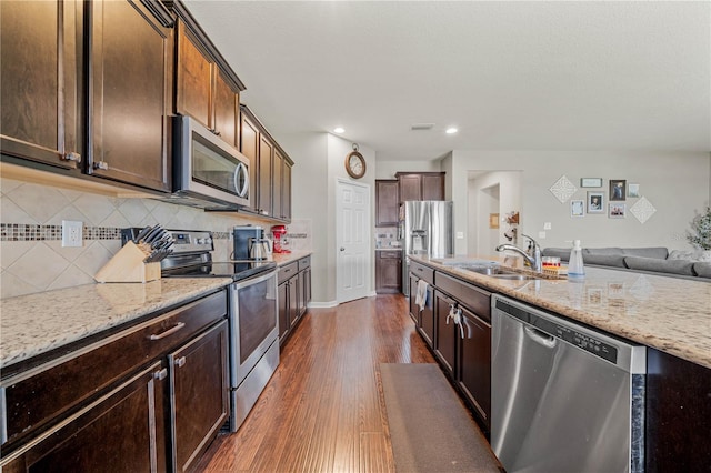 kitchen with stainless steel appliances, sink, light stone counters, decorative backsplash, and dark hardwood / wood-style flooring