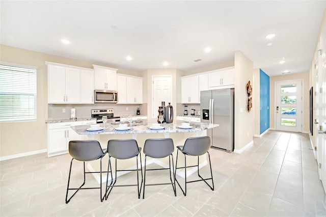 kitchen with appliances with stainless steel finishes, white cabinets, a center island with sink, and light tile patterned floors