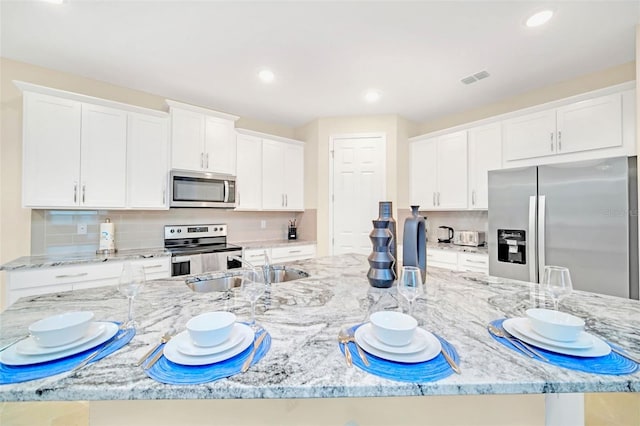 kitchen featuring tasteful backsplash, stainless steel appliances, sink, light stone counters, and white cabinetry