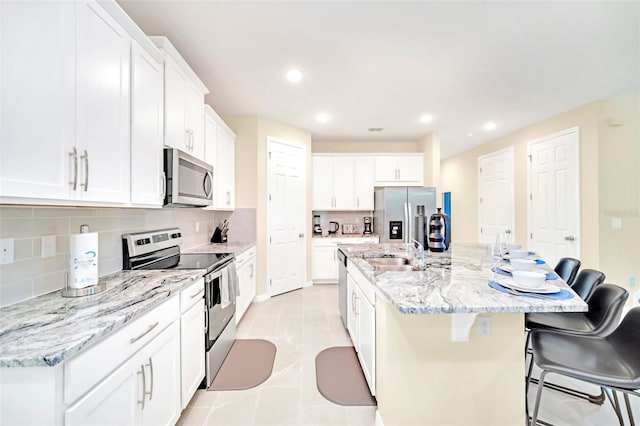 kitchen featuring white cabinetry, an island with sink, a kitchen bar, appliances with stainless steel finishes, and light tile patterned floors